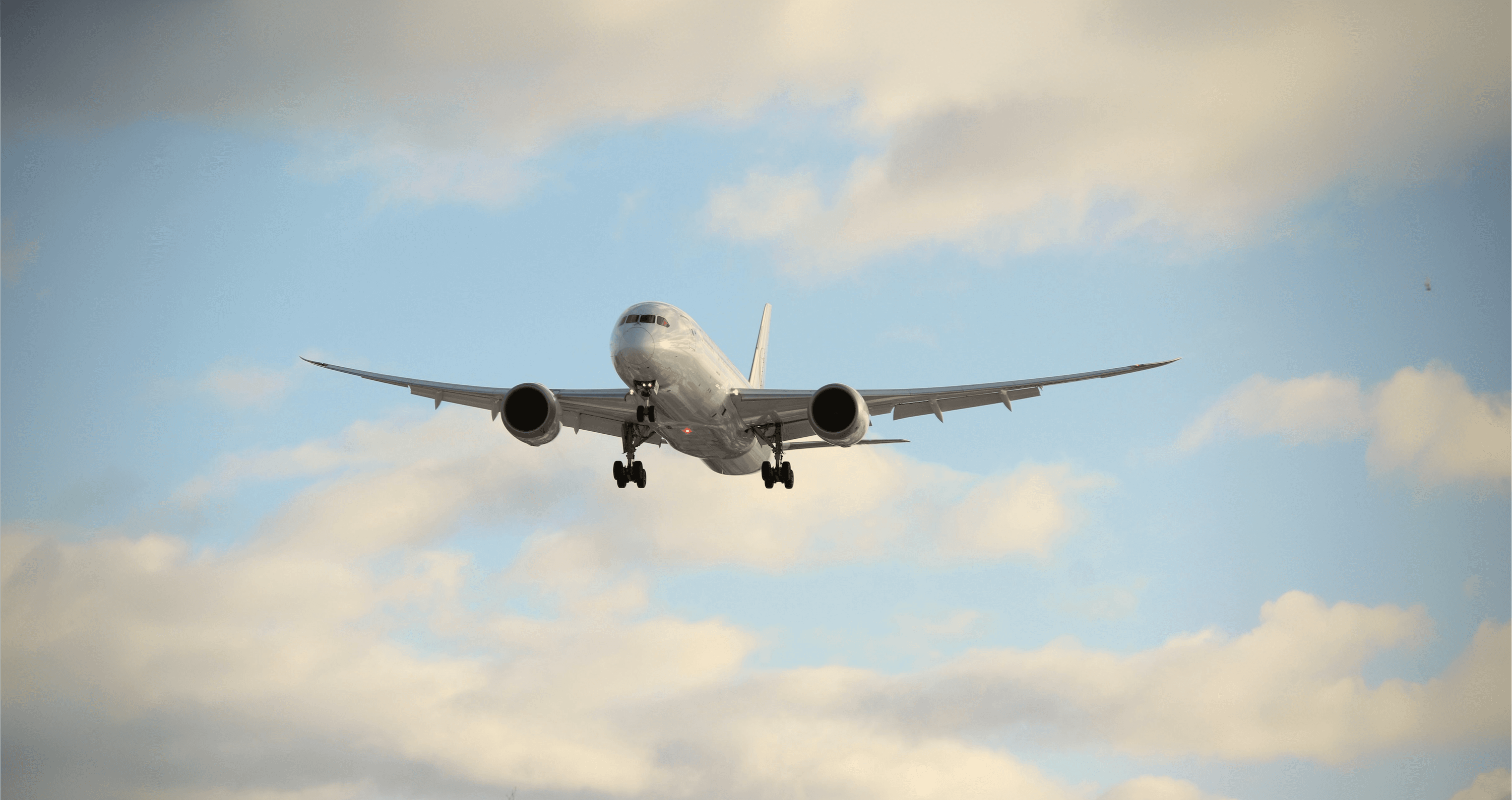 A Boeing 787 climbing through a blue sky with clouds.
