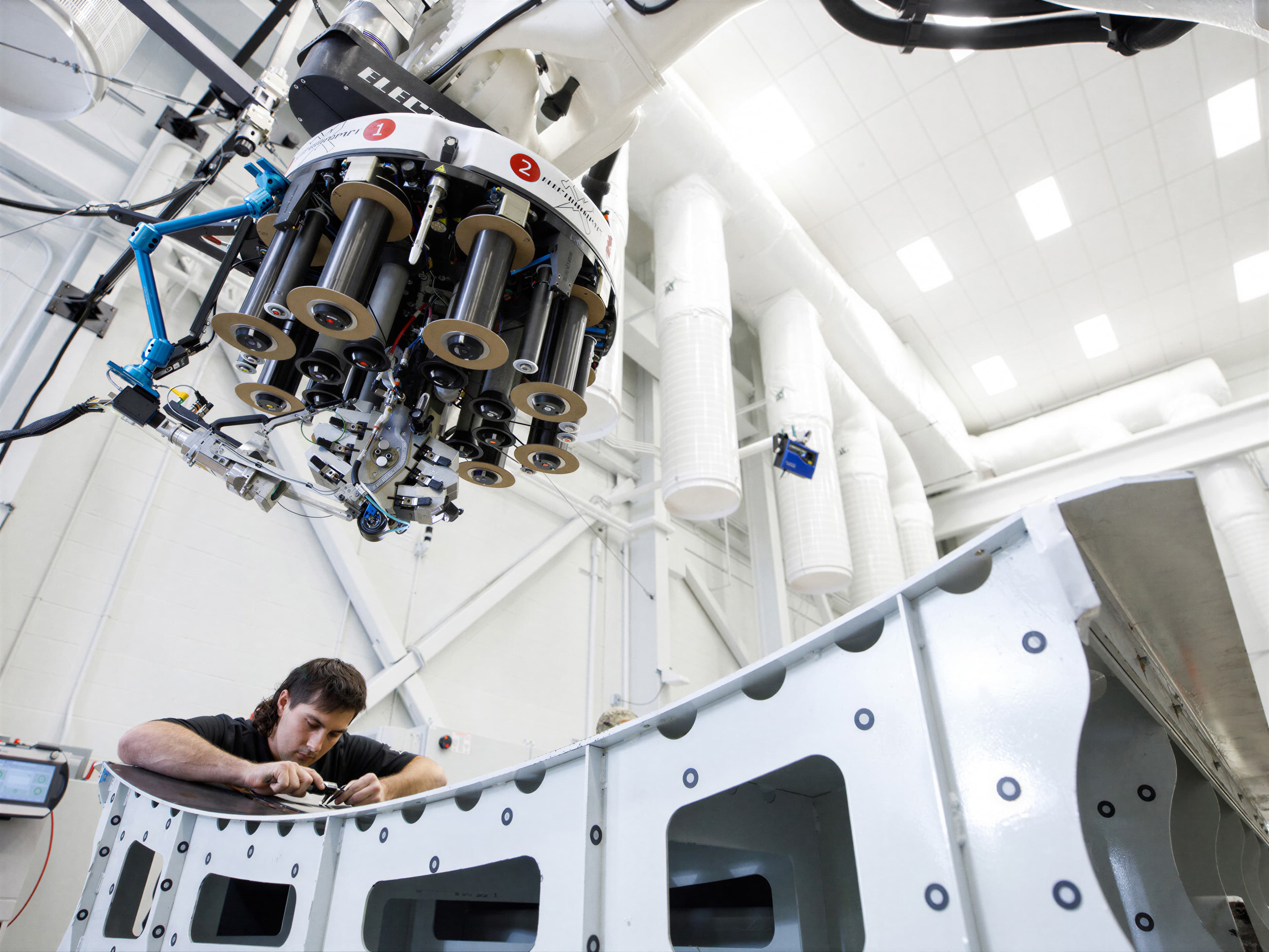 A technician working inside a composite fuselage barrel beneath an inspection head
