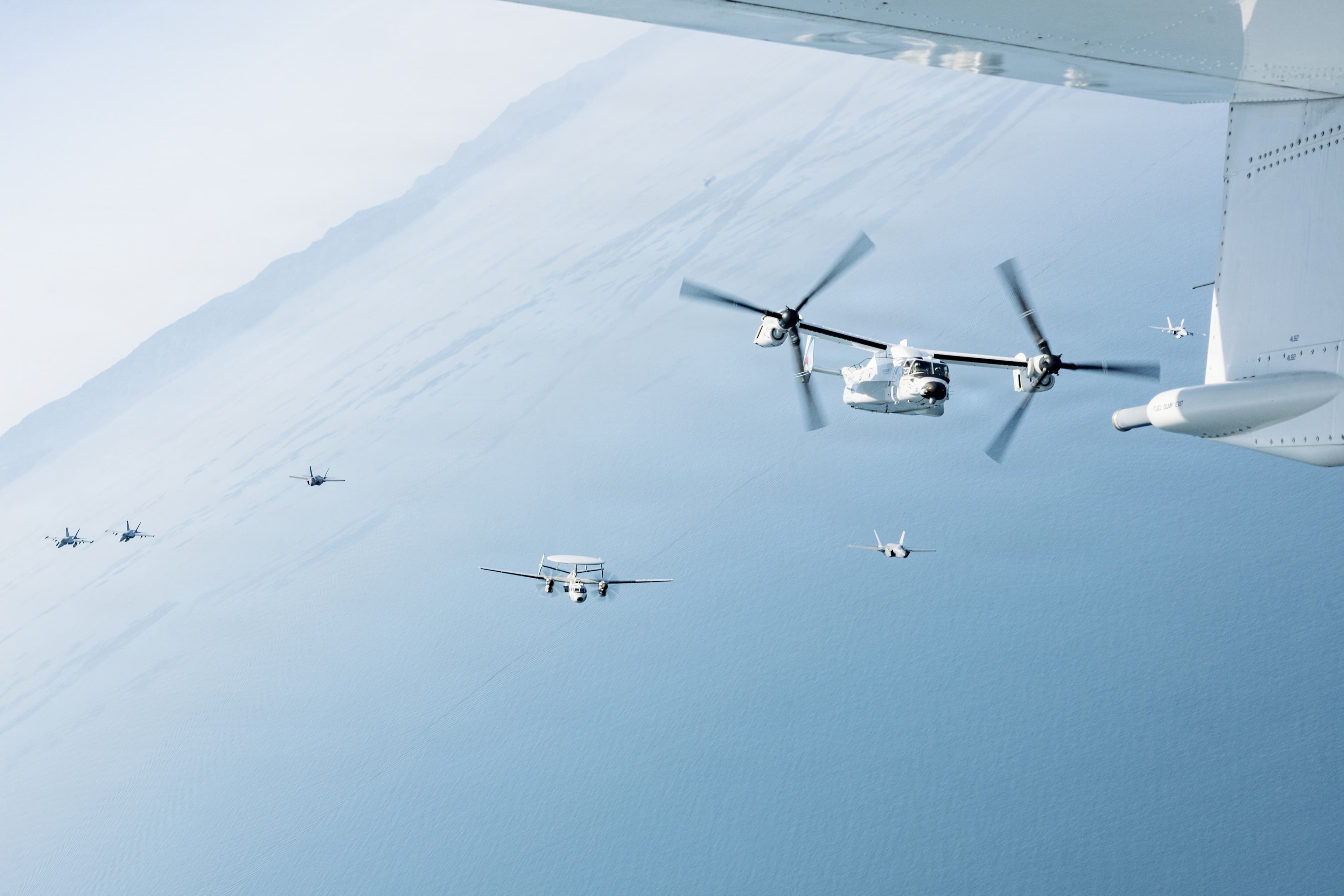A V-22 Osprey flying in formation with escort aircraft